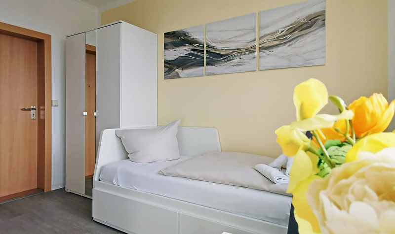 Helles Zimmer mit Bett, Wandbildern und Strauß Blumen