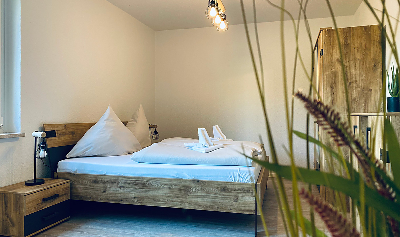 Gemütliches Schlafzimmer, Möble in Holzoptik, im Vordergrund Grünpflanze